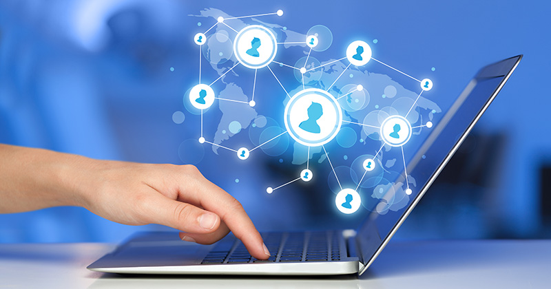 A profile view of a hand at a laptop. Above the laptop is an overlaid graphic of interconnected icons representing people connected through social media.