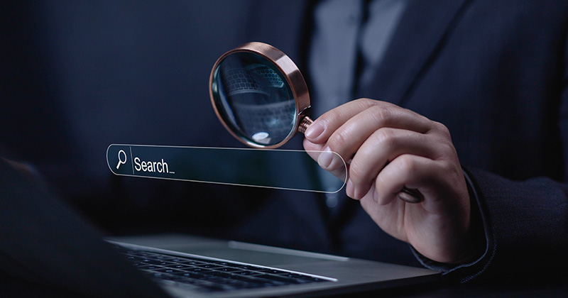 A man holding a magnifying glass up to represent searching online.