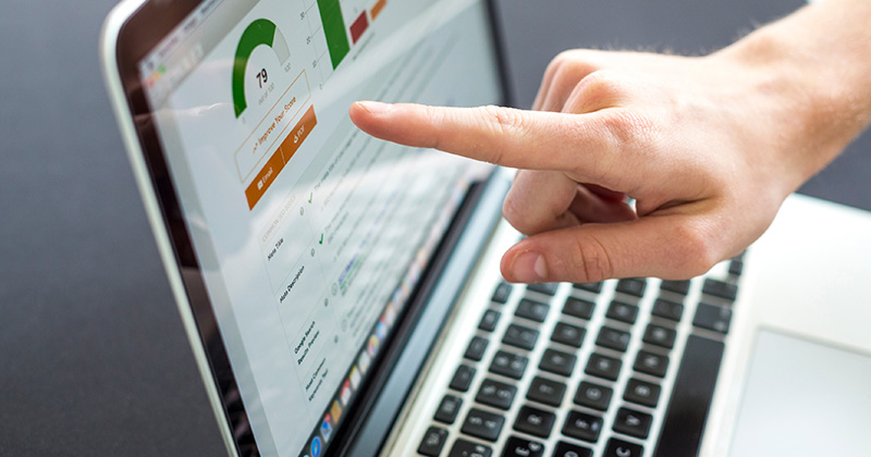 A person pointing at a laptop screen that displays icons representing SEO performance metrics.