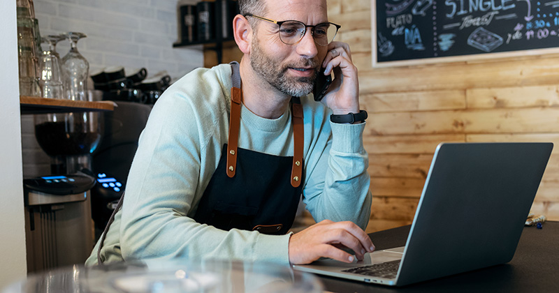 Propietario de empresa que trabaja con un portátil mientras habla por teléfono.