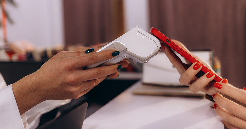 Un iPhone touchant un lecteur de carte pour payer par le biais du traitement de paiement Tap-to-Pay.