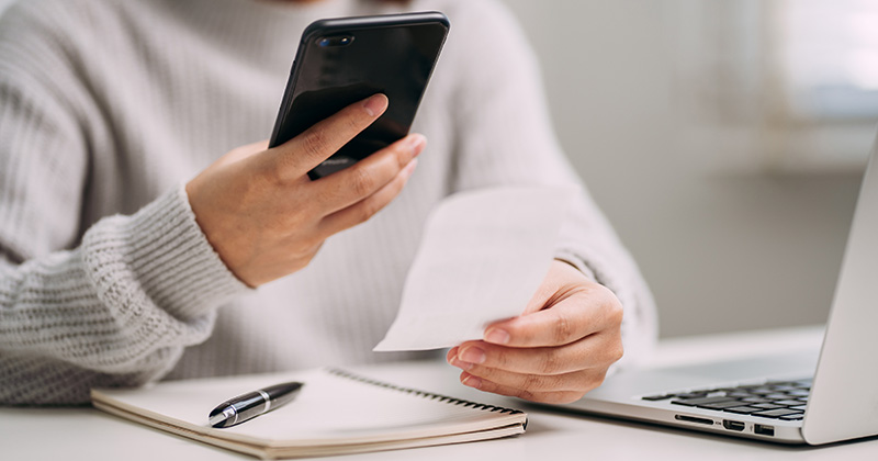 A-young-woman-at-a-desk-uses-her-smart-phone-to-scan-a-paper-receipt-to-create-an-expense-report.