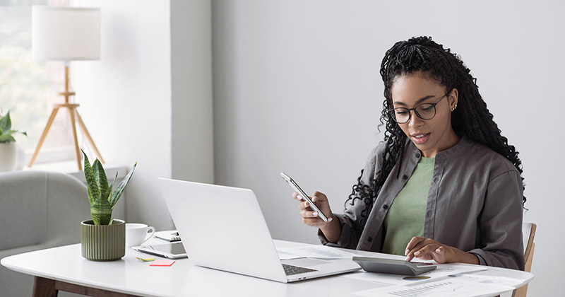 A-young-African-American-woman-sits-at-a-desk-with-a-laptop-and-calculator-working-on-business-accounting.