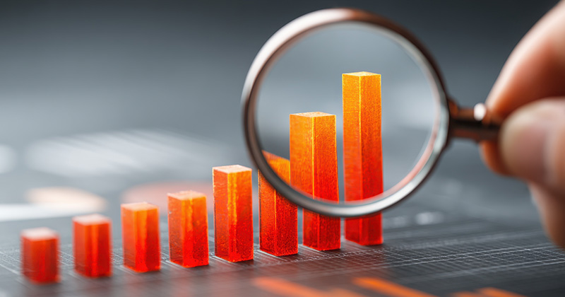 Una lupa enfoca un gráfico de barras naranja 3D que muestra las tendencias al alza de los datos en una pantalla digital.
